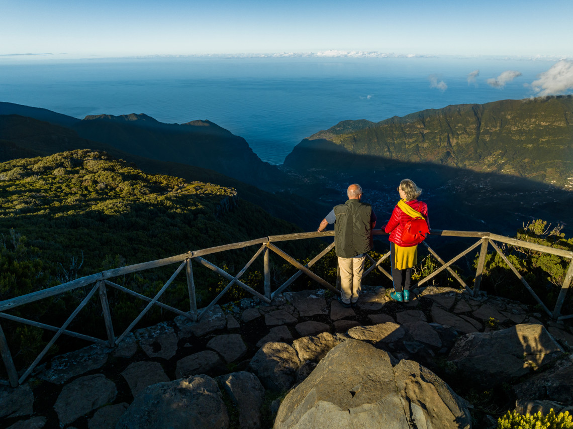Visitors look out from Bica da Cana Viewpoint on Madeira Island, Portugal, over deep mountain valleys, forested slopes, and the Atlantic Ocean. The image shows a wooden lookout terrace in Madeira&rsquo;s highland landscape.