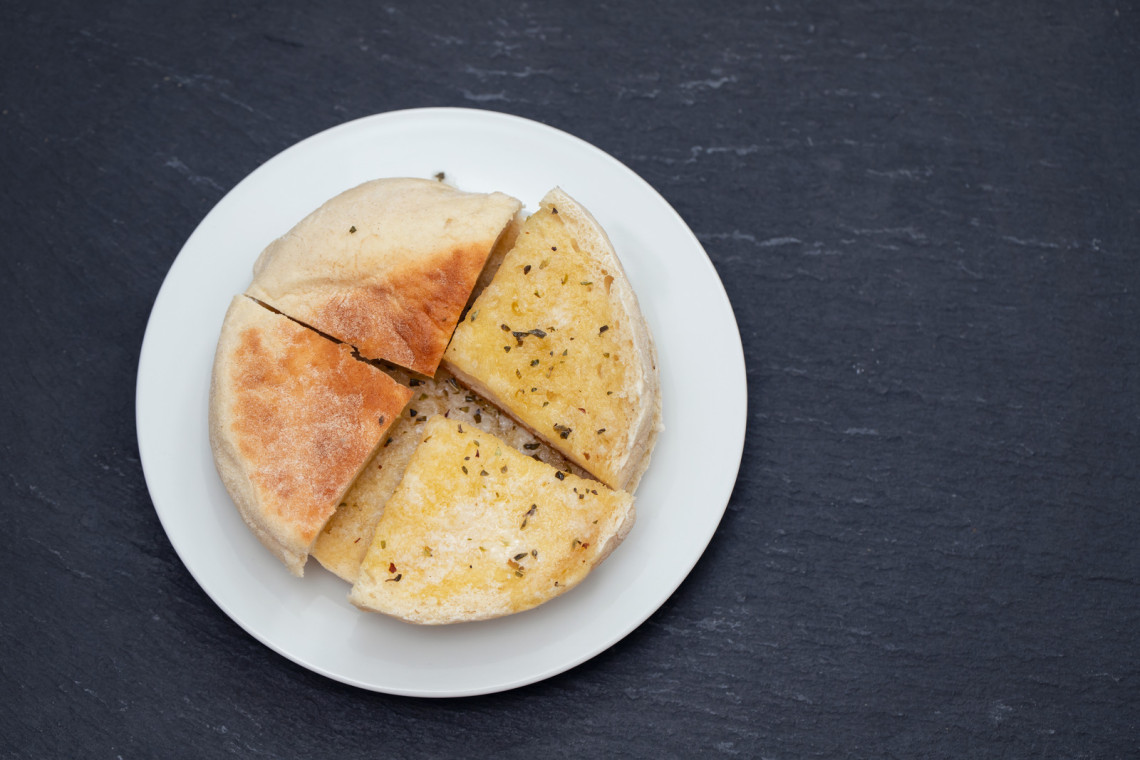 Bolo do Caco from Madeira Island, Portugal, served sliced on a plate with garlic butter and herbs. The image shows a traditional Madeiran flatbread commonly served warm as a side dish or appetizer.