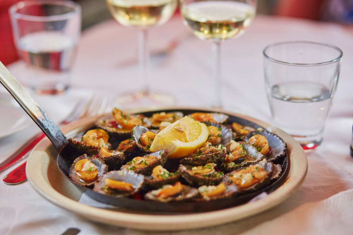 Lapas, or grilled limpets, served on Madeira Island, Portugal, with garlic butter, herbs, and lemon. The image shows a traditional Madeiran seafood starter served in a hot pan at a restaurant table.