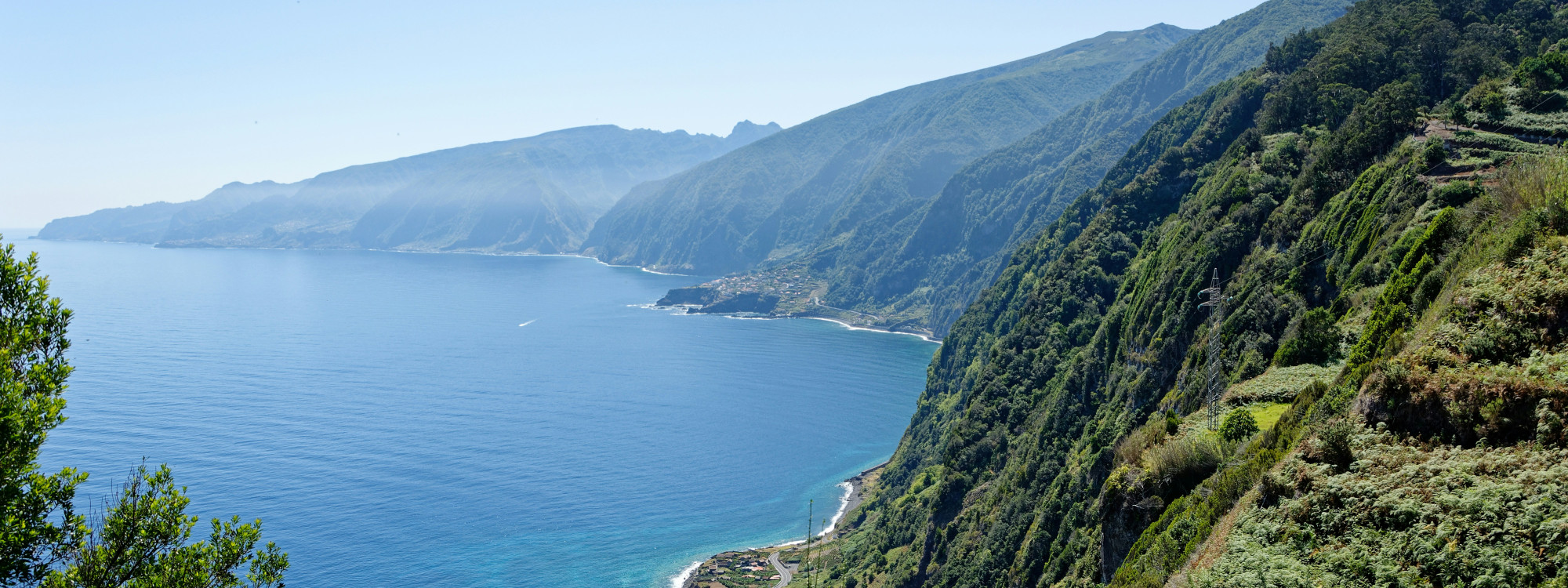 A panoramic view of Madeira Island’s north coast in Portugal, with steep green cliffs descending toward the Atlantic Ocean. The image shows the island’s mountainous shoreline, coastal villages, and blue sea views.