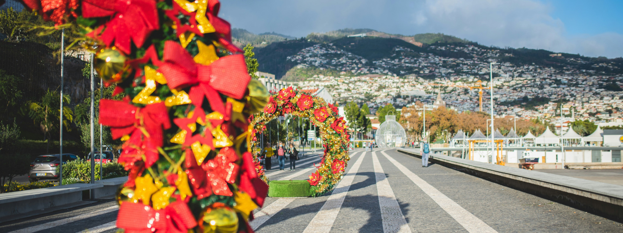 Christmas decorations line the waterfront promenade in Funchal, Madeira, Portugal, with the city’s hillside neighborhoods in the background. The image highlights Madeira’s festive season atmosphere near the Atlantic coast.