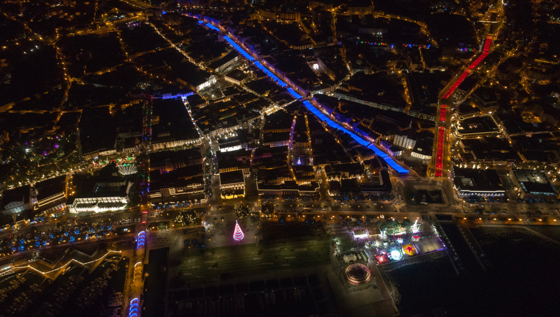 Aerial night view of the Funchal waterfront in Madeira, Portugal, showing the illuminated marina, Avenida do Mar, and the city center decorated with festive lights. The image captures Funchal's coastal layout and vibrant urban atmosphere from above.