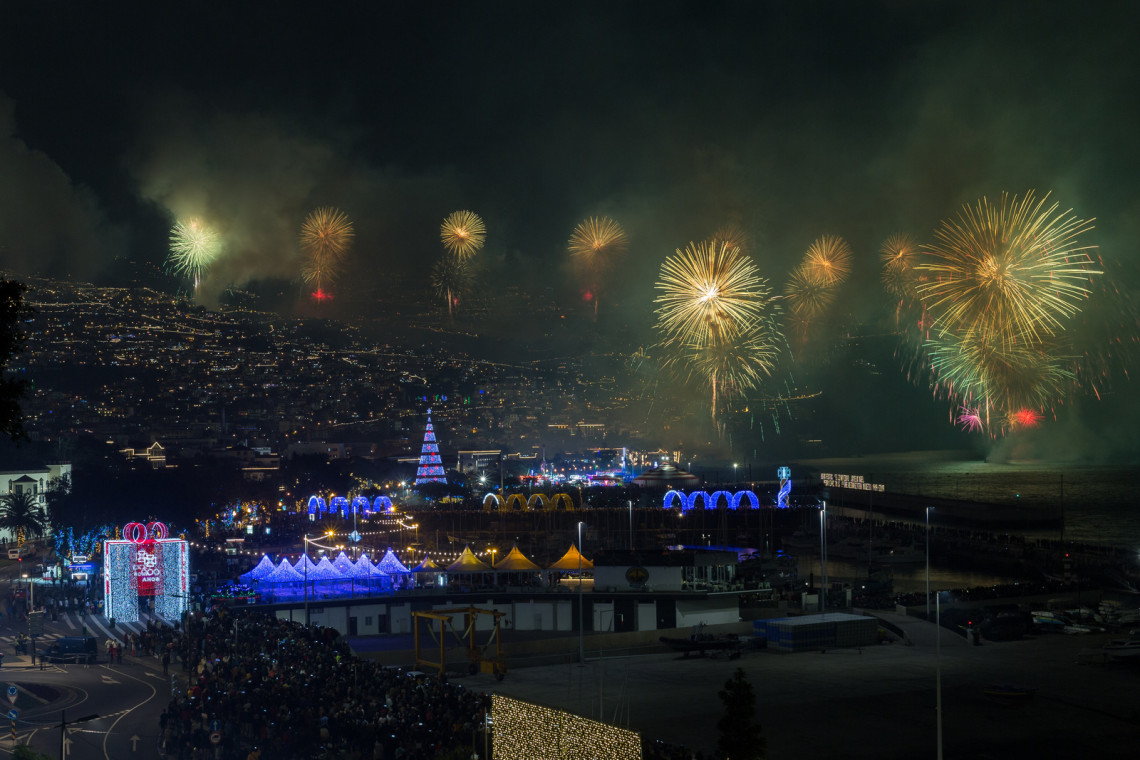 Fireworks illuminate the coastline of Funchal, Madeira, Portugal, during the city&rsquo;s New Year&rsquo;s Eve celebrations. Festive lights, crowds, and waterfront installations fill the foreground beneath the hillside cityscape.
