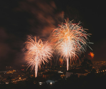 Fireworks light up the night sky over Funchal, Madeira, Portugal, with the city and coastline visible below. The image highlights an evening celebration and festive atmosphere on the island.