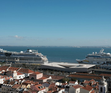 Cruise ships docked at Lisbon Cruise Port along the Tagus River, with the terracotta rooftops and historic buildings of central Lisbon in the foreground.