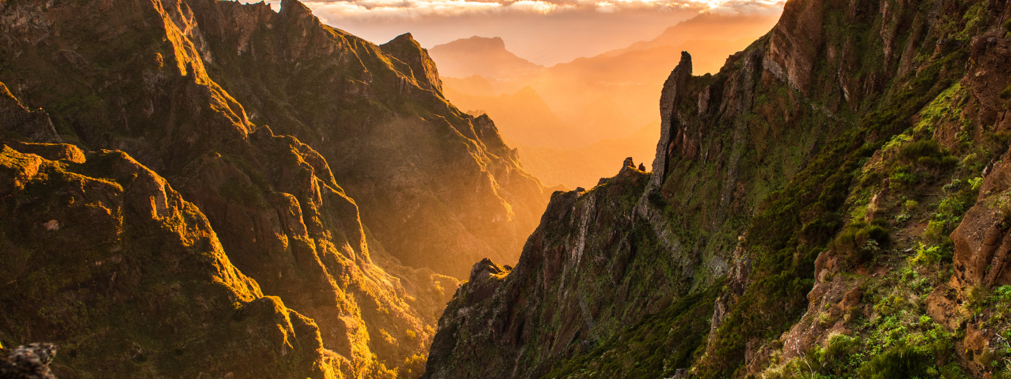 Sunrise light fills the rugged volcanic valleys near Pico do Arieiro in Madeira, Portugal. Steep rock formations and layered mountain ridges create a dramatic view across the island’s central highlands.