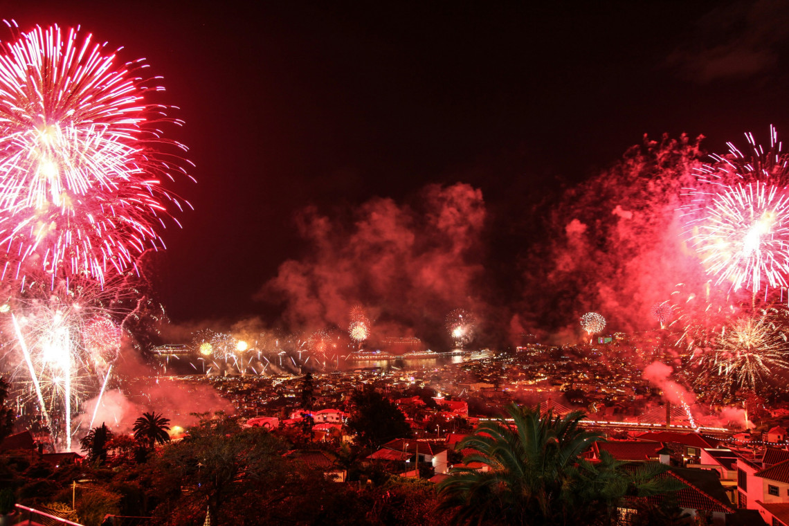 New Year&rsquo;s Eve fireworks illuminate Funchal and its bay on Madeira Island, Portugal. Red and white bursts rise above the city&rsquo;s hillside neighbourhoods, rooftops and palm trees during the annual celebration.