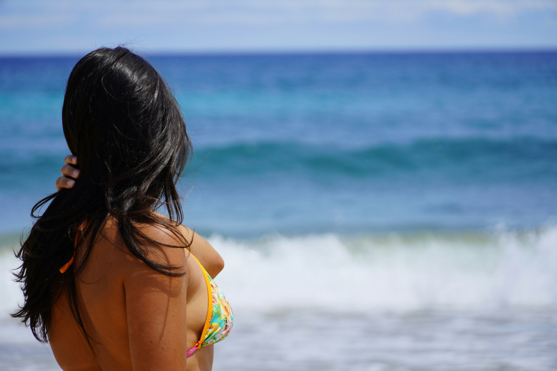 A woman in swimwear looks toward the Atlantic Ocean from Porto Santo Beach near Vila Baleira, Portugal. Blue water and breaking waves fill the background along the island&rsquo;s golden sand coastline.