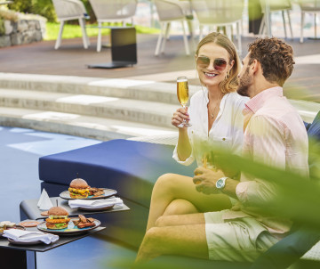 A couple enjoys drinks and light food at a hotel poolside area in Funchal, Madeira Island, Portugal. The image shows a romantic resort-style stay with relaxed outdoor dining and warm-weather leisure.