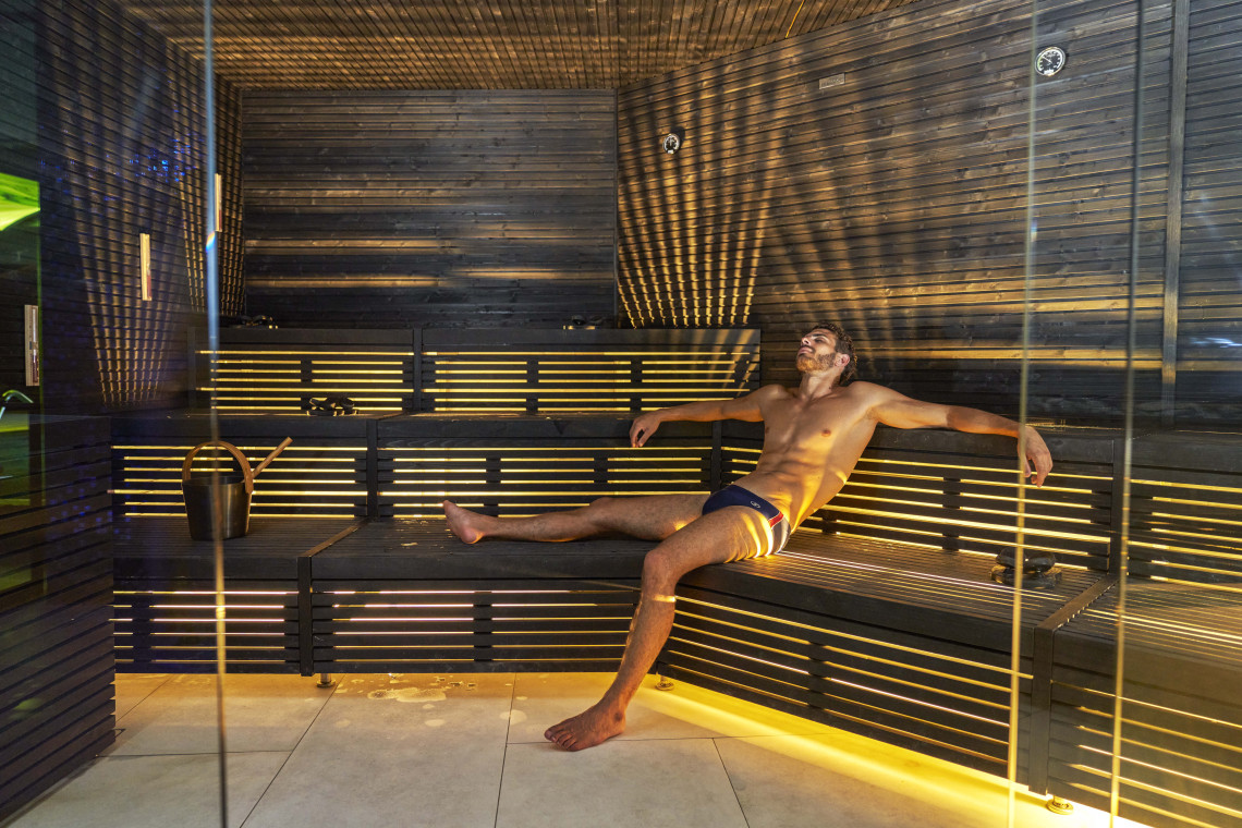 A traveler relaxes inside a sauna in Funchal, Madeira, Portugal, surrounded by wooden interiors and warm lighting. The image highlights a hotel wellness experience during a Madeira holiday.