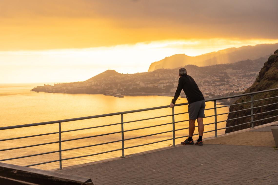 A visitor looks across the Atlantic coastline from Cristo Rei Viewpoint in Cani&ccedil;o, Madeira, Portugal, during sunset. The elevated viewpoint offers wide views toward Funchal, the surrounding hills, and the island&rsquo;s southern coast.