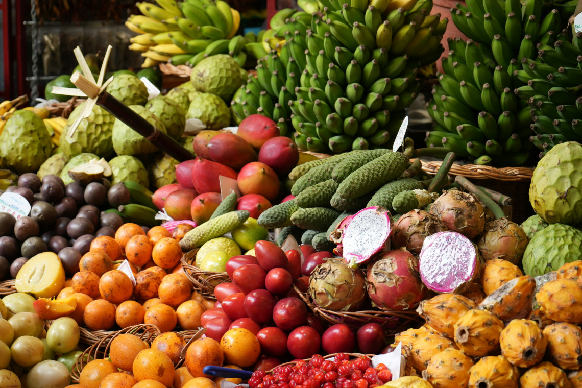 A colorful display of tropical fruits and local produce at Mercado dos Lavradores in Funchal, Madeira, Portugal. Bananas, custard apples, passion fruit, dragon fruit, and other regional products fill the market stall.