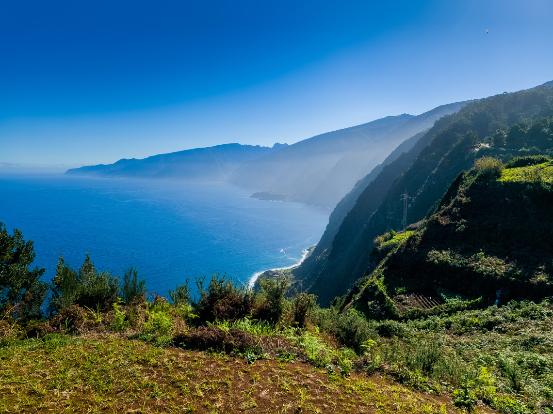 View of Madeira's rugged north coast with layered cliffs, terraced hillside, and misty ocean in the distance