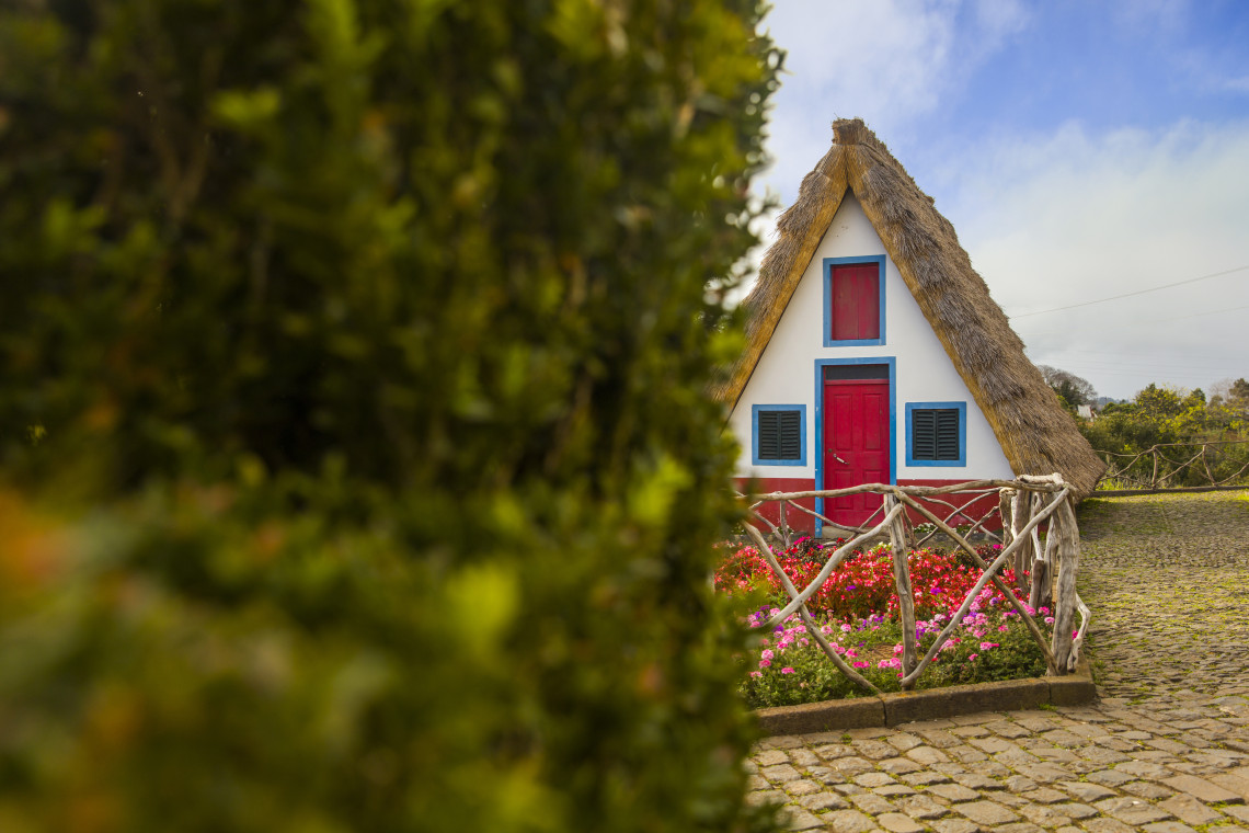 Traditional triangular Santana house with thatched roof, red door, and blue trim in Madeira