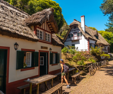 Traditional Madeira village with whitewashed stone houses, red-trimmed windows, terracotta tile roofs, cobblestone paths, and lush green vegetation on hillside in Madeira Island, Portugal