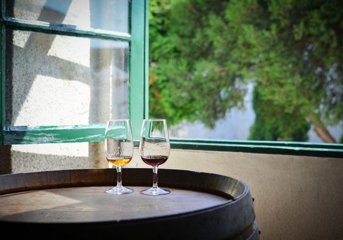 Two glasses of port wine, one tawny and one ruby, resting on a wine barrel by a window in the Douro Valley