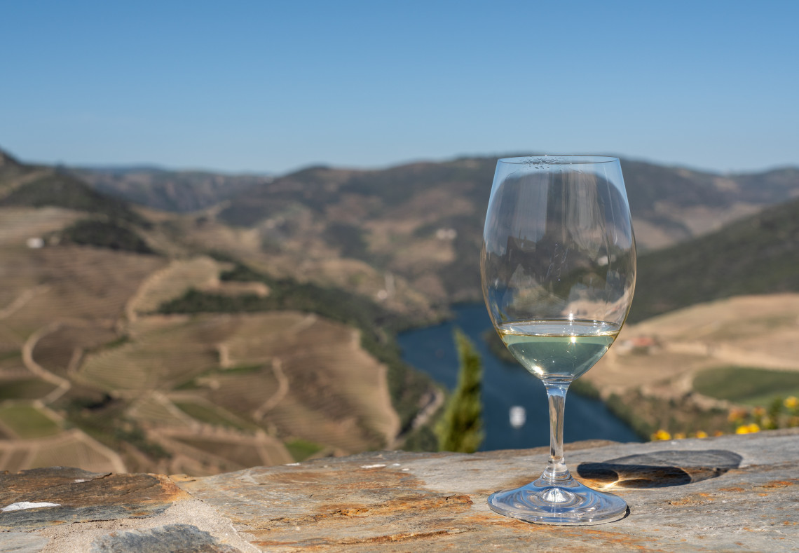 Glass of white wine on a stone ledge overlooking the Douro River and terraced vineyard hillsides