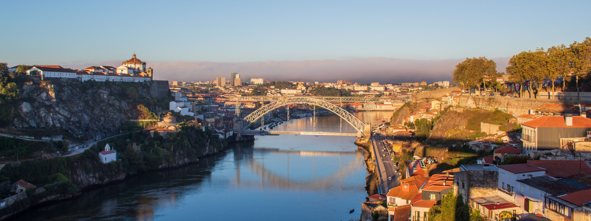 The Dom Luís I Bridge spans the Douro River between Porto and Vila Nova de Gaia, Portugal. Historic riverside buildings and the elevated Monastery of Serra do Pilar surround the iron arch bridge.