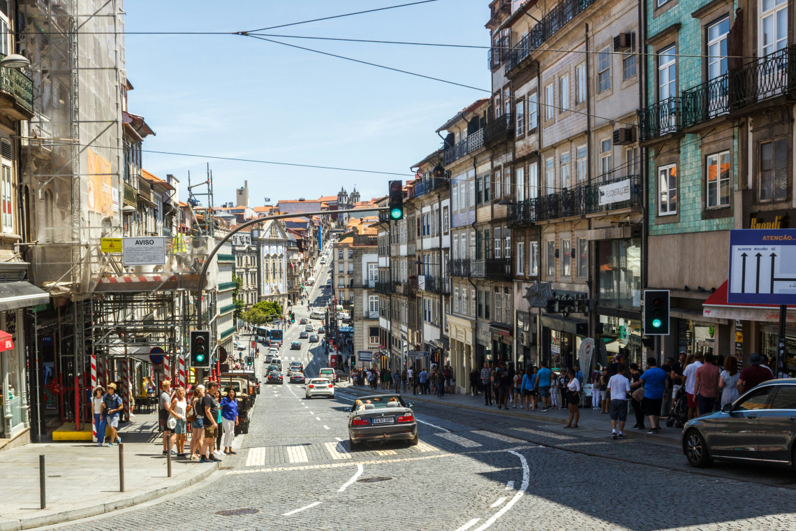 View of Rua de 31 de Janeiro in Porto, Portugal, with traditional buildings, tram wires, traffic, and pedestrians in the city center. The image shows everyday street life in Porto&rsquo;s historic downtown area.