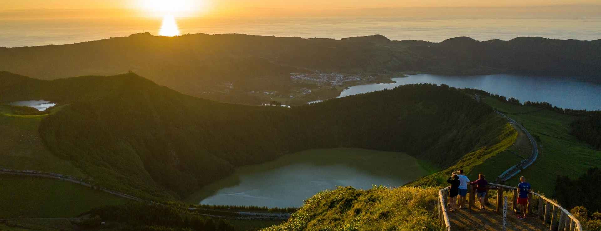 Aerial golden hour view of the Sete Cidades crater lakes on São Miguel Island, Azores, with warm orange sunset light reflecting on the water and green volcanic hillsides in shadow