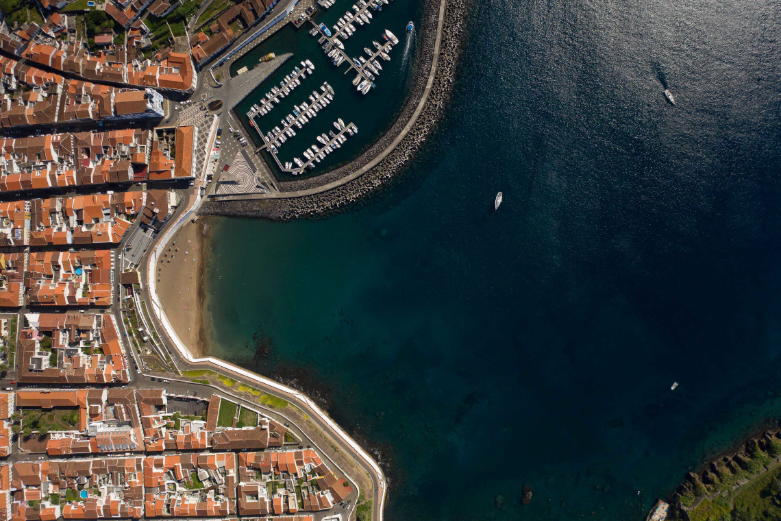 Aerial top-down view of Prainha beach and marina in Angra do Hero&iacute;smo, with terracotta rooftops and deep blue Atlantic Ocean, Terceira Island, Azores