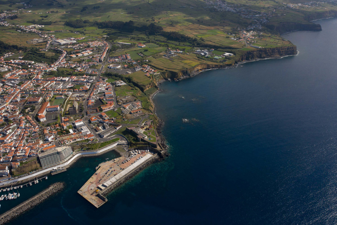 Aerial view of Angra do Hero&iacute;smo in Terceira Island, Azores, showing the historic town, marina, harbor, and dramatic coastline beside the deep blue Atlantic Ocean.