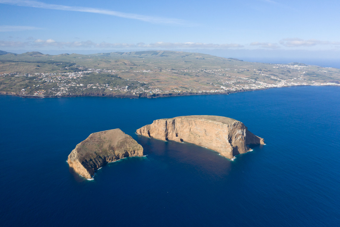 Aerial view of Ilh&eacute;us das Cabras off the coast of Terceira Island, Azores, Portugal. The twin volcanic islets rise from the Atlantic Ocean with the island's coastline and surrounding landscape visible in the background.