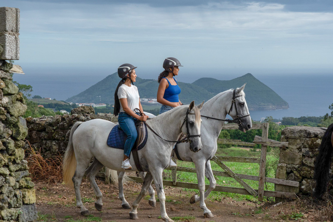 Visitors enjoying a horseback riding tour on Terceira Island, Azores, Portugal. The scenic trail overlooks the island's green volcanic landscape and the Atlantic Ocean, offering panoramic coastal views.
