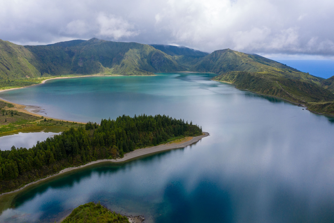 Panoramic view of Lagoa do Fogo on S&atilde;o Miguel Island, showing the blue volcanic crater lake, forested shoreline and steep green ridges beneath low clouds.