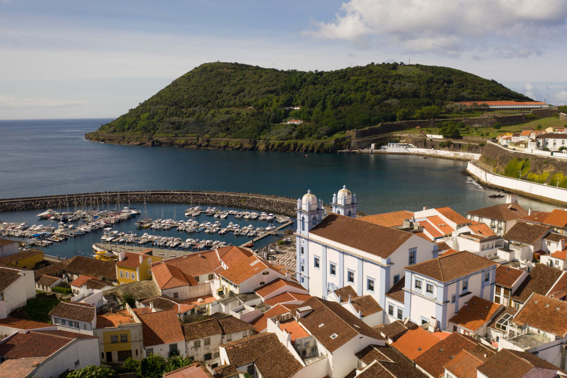 Elevated view over the historic center and marina of Angra do Hero&iacute;smo on Terceira Island, with traditional red-tiled roofs, the waterfront and Monte Brasil rising across the bay.