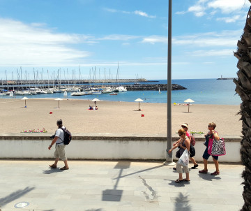 View across the sandy beachfront of Praia da Vitória on Terceira Island, with the marina, sailboats and calm Atlantic waters in the background.
