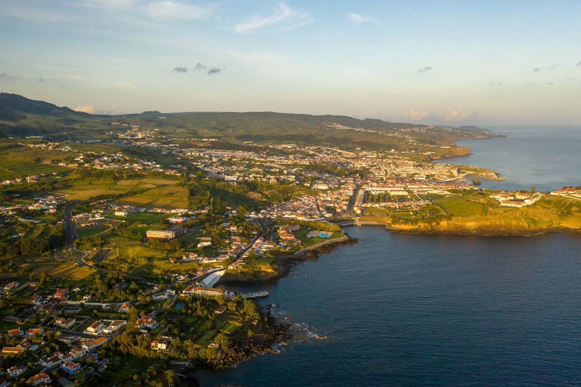Aerial view of Praia da Vit&oacute;ria on Terceira Island in the Azores, Portugal, showing the town extending along the Atlantic coastline. Green fields, residential areas, volcanic headlands and sheltered bays shape the coastal landscape.