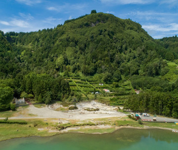 Aerial view of the geothermal area beside Lagoa das Furnas in Furnas, São Miguel Island, Portugal. Pale fumarole fields line the green crater lake beneath densely forested volcanic slopes.