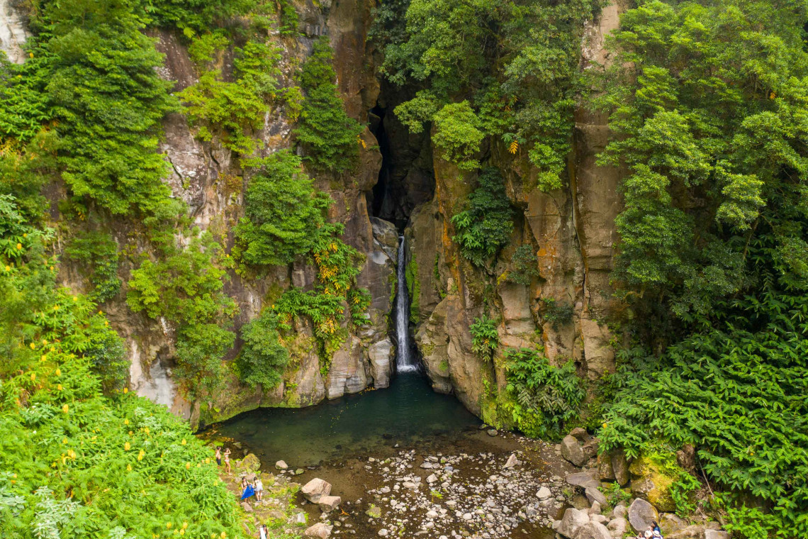 Salto do Cabrito waterfall cascading through a steep volcanic gorge near Ribeira Grande on S&atilde;o Miguel Island, surrounded by dense green vegetation and a natural pool below.