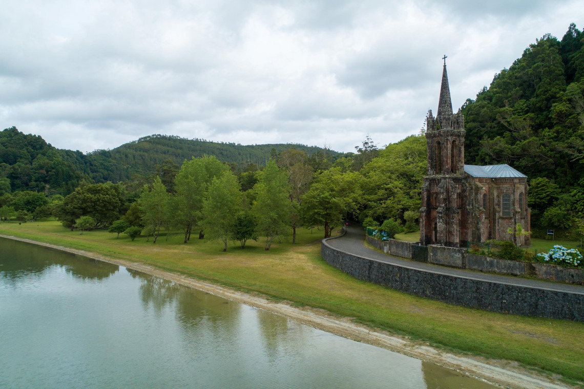 View across Lagoa das Furnas on S&atilde;o Miguel Island, with the forested shoreline and the Gothic-style Capela de Nossa Senhora das Vit&oacute;rias beside the lake.