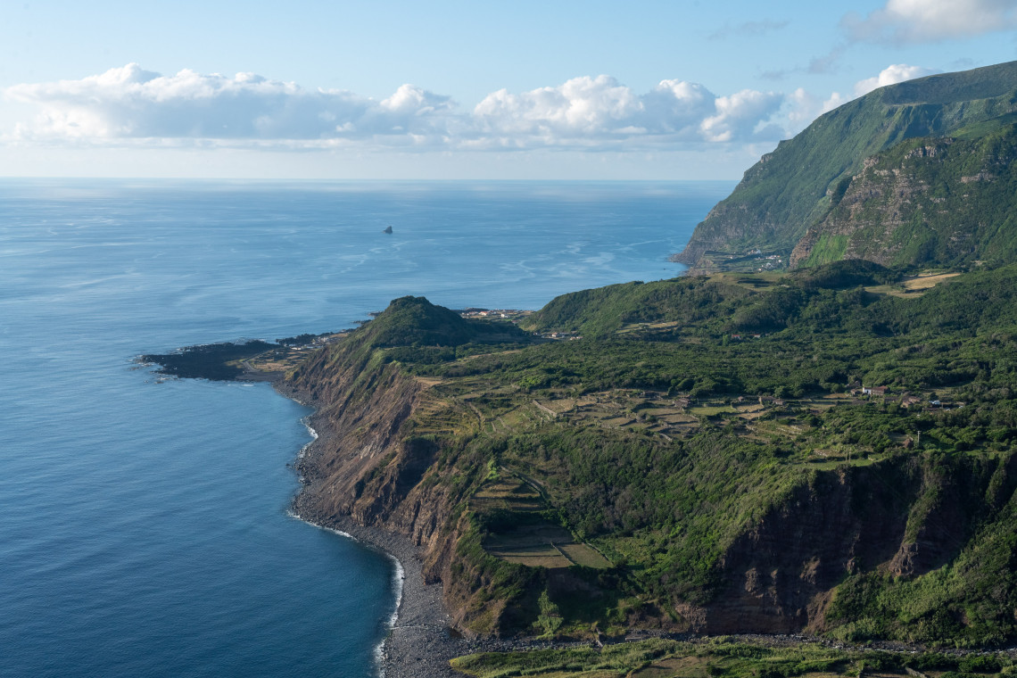 Elevated view of the coastline on Flores Island in the Azores, showing steep volcanic cliffs, green terraced land and the Atlantic Ocean stretching into the distance.