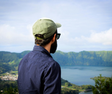 Visitor overlooking Lagoa das Sete Cidades on São Miguel Island, with the blue crater lake and steep green volcanic walls stretching across the landscape.