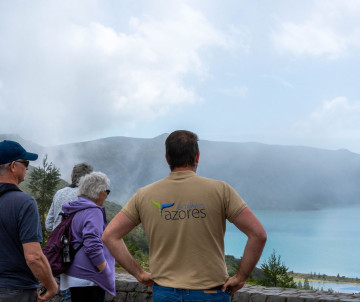 Group of visitors standing at a viewpoint overlooking the turquoise volcanic crater lake of Lagoa do Fogo on São Miguel Island, Azores, with low cloud and mist over the water