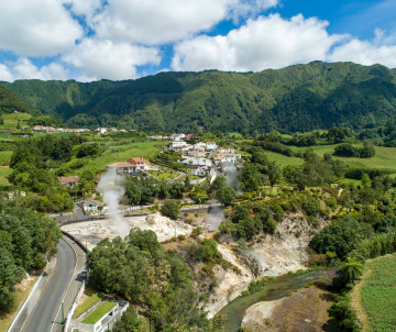 Aerial view of the Furnas geothermal area on São Miguel Island, showing steaming volcanic ground, green vegetation, roads and houses surrounded by the Furnas caldera.