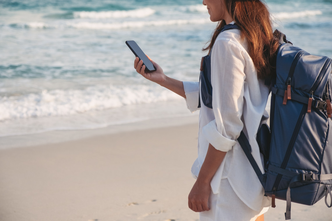 Solo traveler with backpack using a smartphone on a beach in the Azores, highlighting mobile connectivity and travel safety