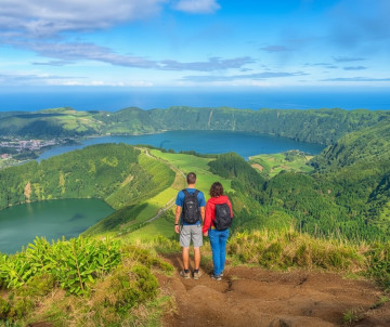 Couple hiking along a viewpoint overlooking Sete Cidades crater lakes surrounded by green hills on São Miguel Island in the Azores