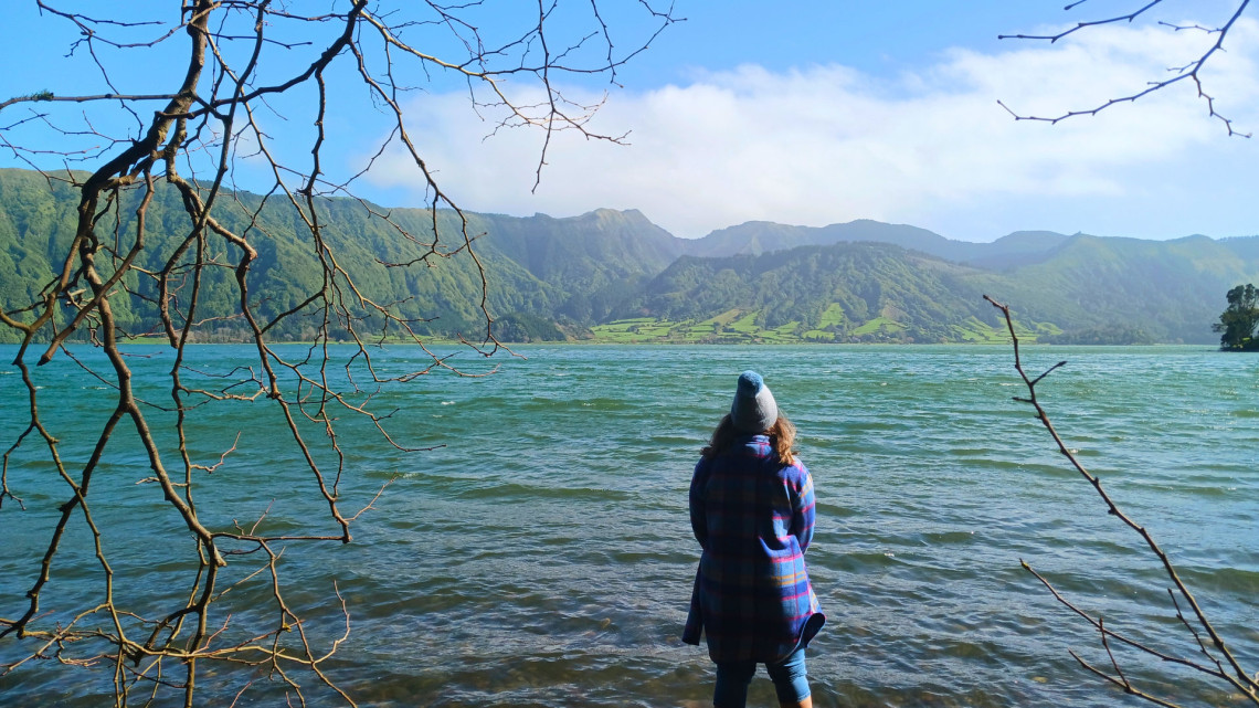 A visitor stands beside the waters of Sete Cidades on S&atilde;o Miguel Island, looking toward the steep green volcanic ridges and cultivated landscape surrounding the caldera.