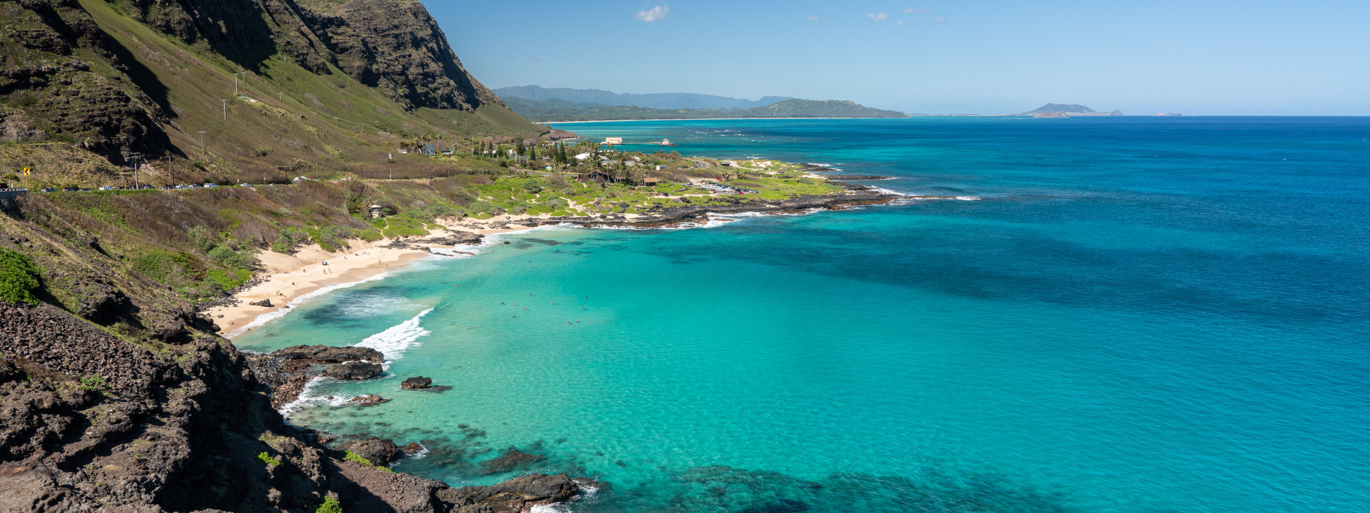 Aerial view of Makapu'u Beach on Oahu's east coast, with turquoise water, volcanic rocky shoreline, green sea cliffs, and Rabbit Island visible in the distance