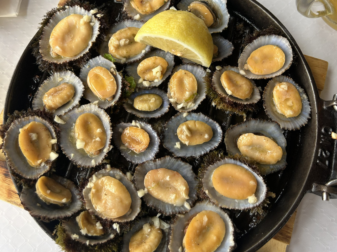 Cast iron pan of grilled limpets with garlic and lemon served on a wooden board on S&atilde;o Miguel Island, Azores &mdash; a traditional Azorean seafood dish