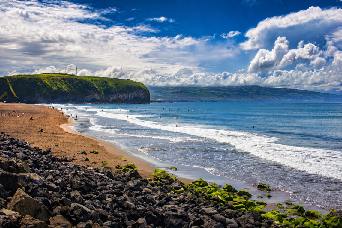 Wide sandy beach at Praia de Santa B&aacute;rbara with Atlantic waves rolling in, green headland, and dramatic cloudy sky, north coast of S&atilde;o Miguel Island, Azores