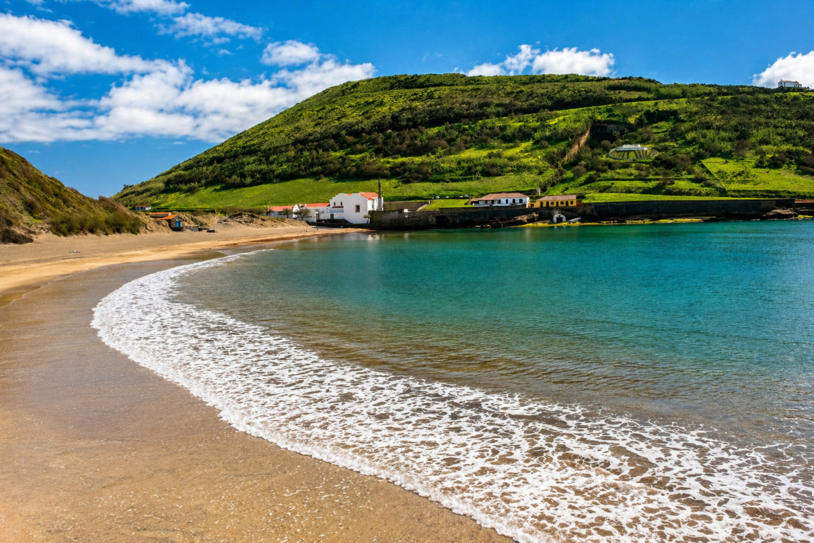 Crescent of golden sand at Praia do Porto Pim in a sheltered bay near Horta, with green hillside and calm turquoise Atlantic water, Faial Island, Azores