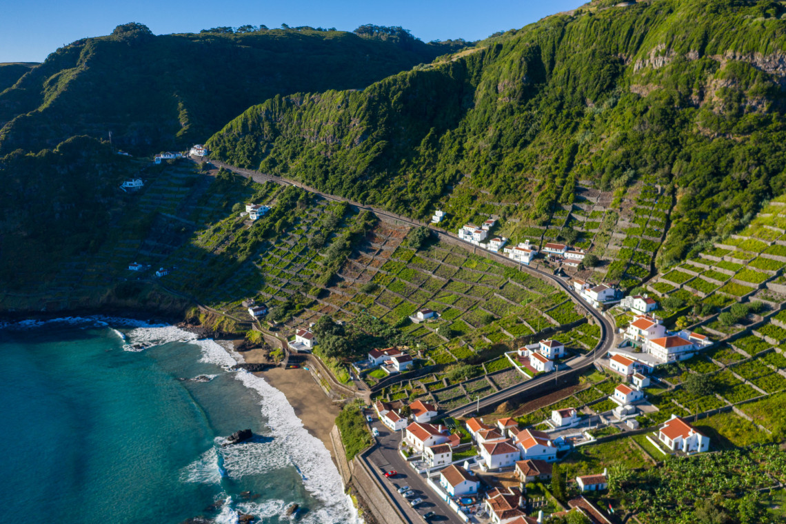 Aerial view of Praia de S&atilde;o Louren&ccedil;o sheltered cove with turquoise Atlantic water, golden sand, and dramatic reddish volcanic cliffs, Santa Maria Island, Azores