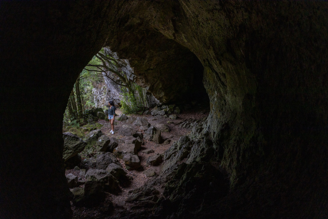 Traveler exploring Furna da Maria Encantada on Graciosa Island, framed by the dark walls and rocky floor of the volcanic lava cave near the rim of the Caldeira.