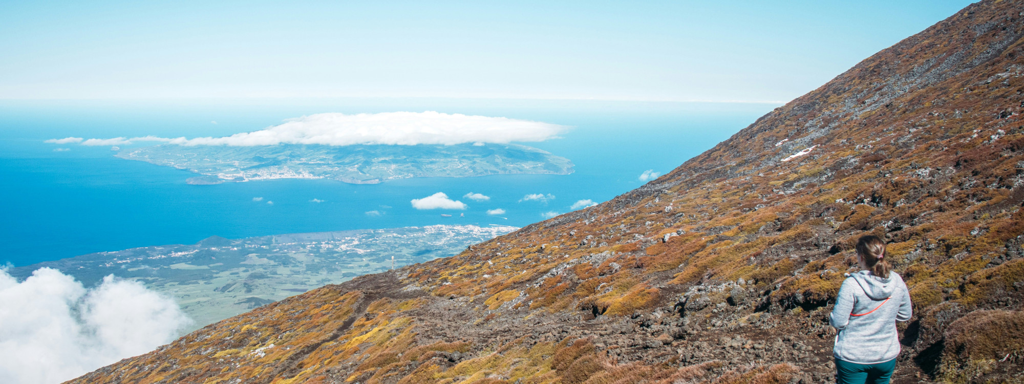 Hiker on the rocky slopes of Mount Pico overlooking the Atlantic Ocean and neighboring Faial Island during the ascent on Pico Island.