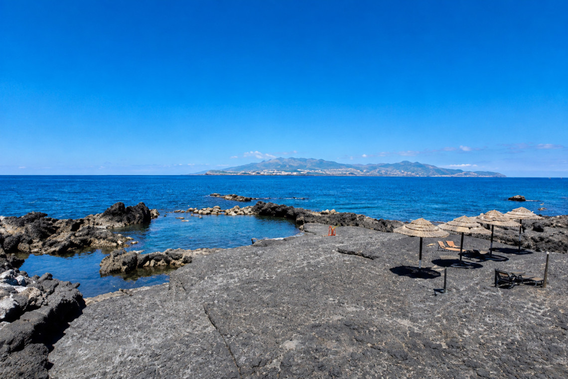 Laja das Rosas natural pools in Cria&ccedil;&atilde;o Velha on Pico Island, with black volcanic rock, ocean swimming areas and straw sun umbrellas overlooking the Atlantic. The site lies within Pico Island&rsquo;s UNESCO-listed Vineyard Culture landscape.